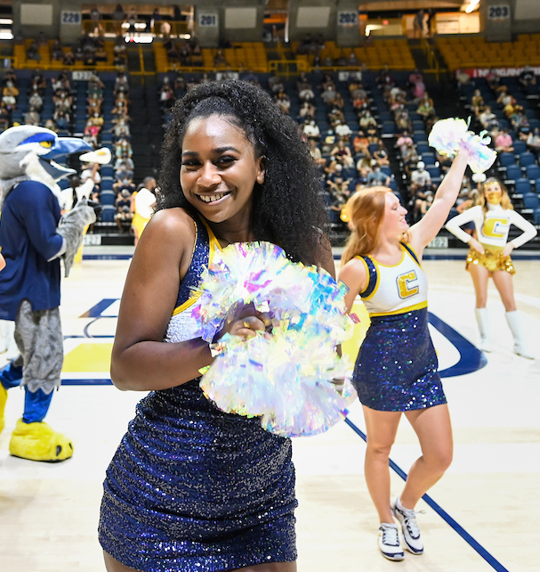 Dancers perform on the McKenzie Arena floor. One smiles at the camera, holding pom-poms.