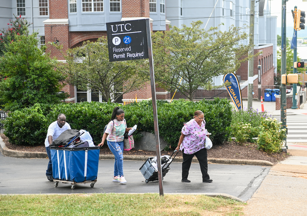 Family walks near UTC parking sign, carrying bags and pushing a cart during Operation Move-In.