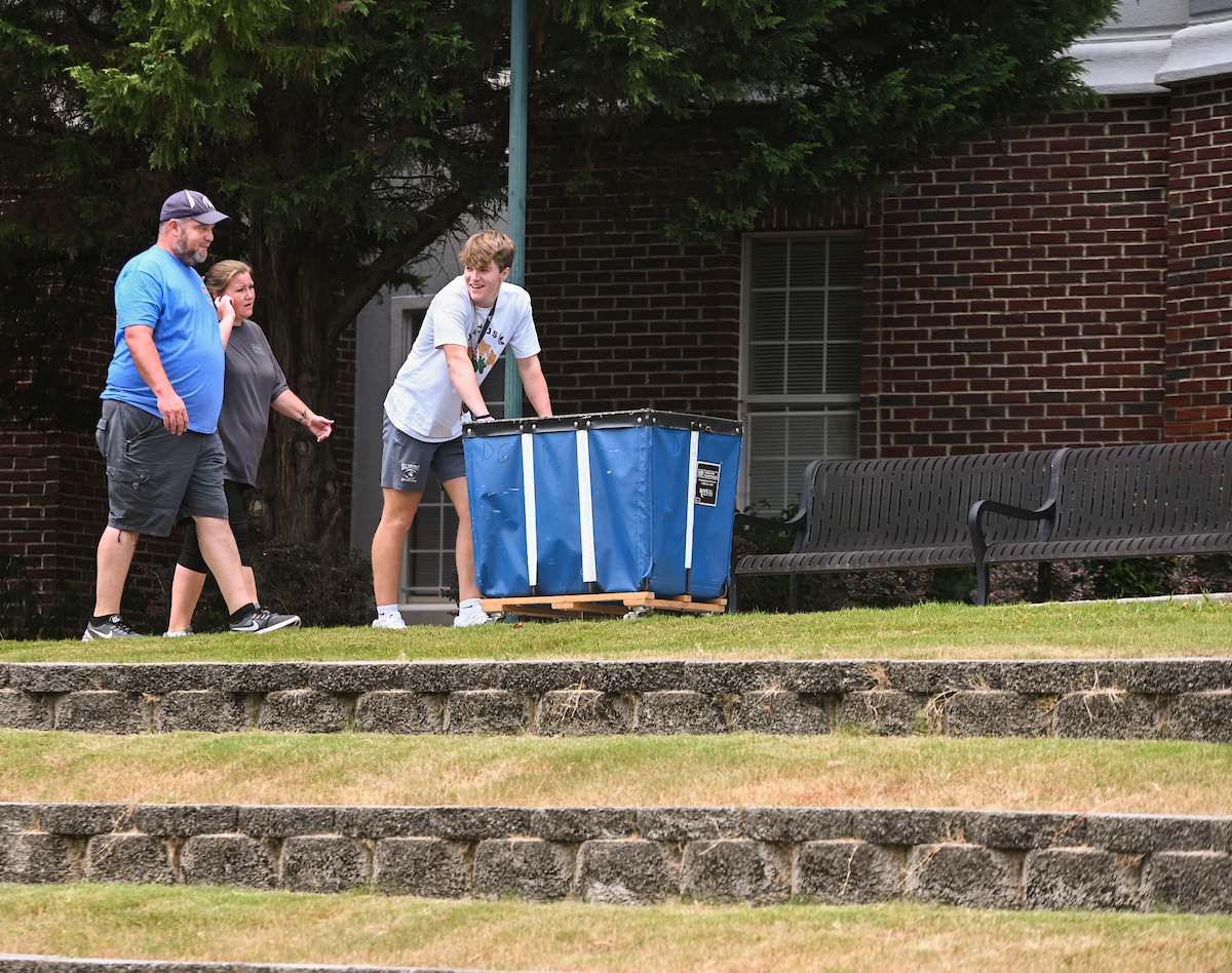 A family moving large blue cart outdoors, during Operation Move-In.