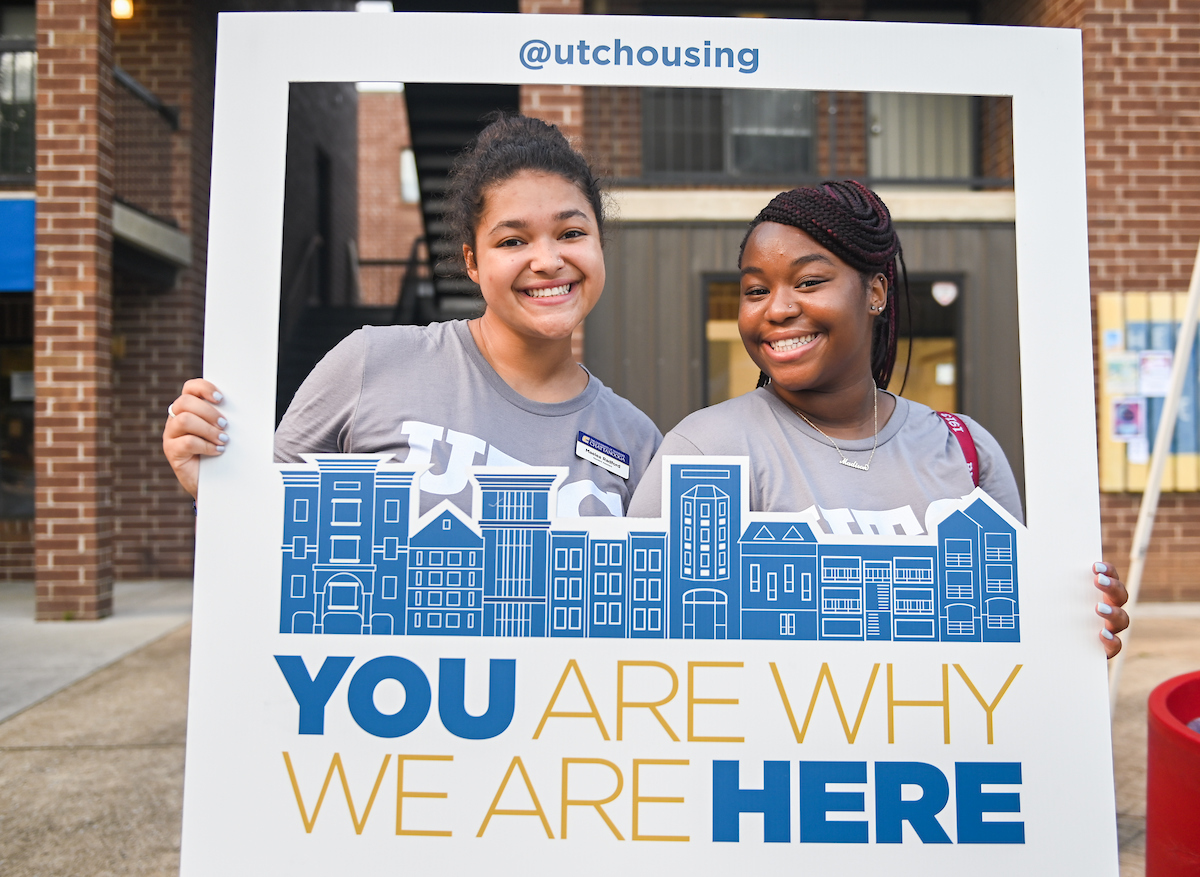 Students smiling and holding frame with text "@utchousing" and "YOU ARE WHY WE ARE HERE" in blue and gold.