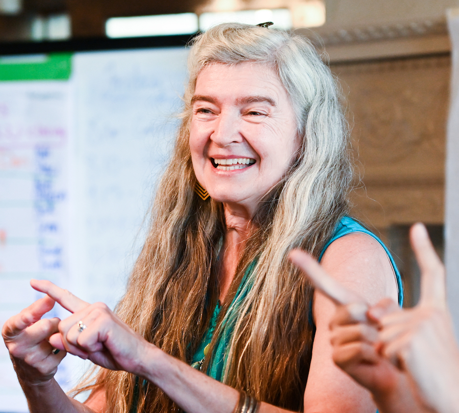 A smiling woman gestures happily with both hands.