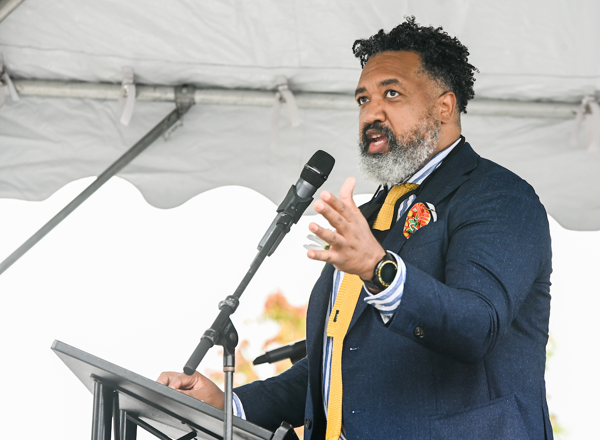 Donivan Brown speaks at a podium under a tent, gesturing with his hand.