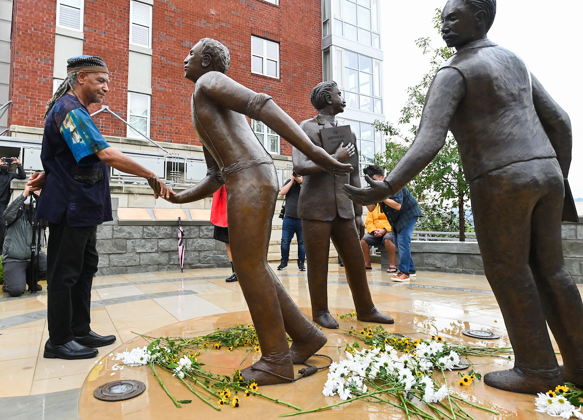 A man shakes hands with a bronze statue in a circle of figures on a wet plaza.
