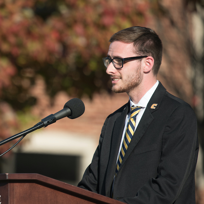 A man in a suit speaks outside at a podium.