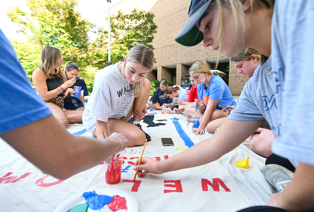 A group of students paint a banner outdoors.