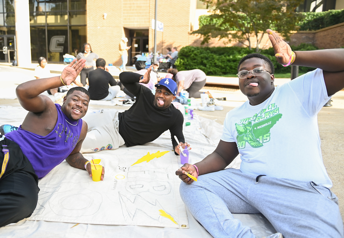 Three people pose playfully while painting on a banner.