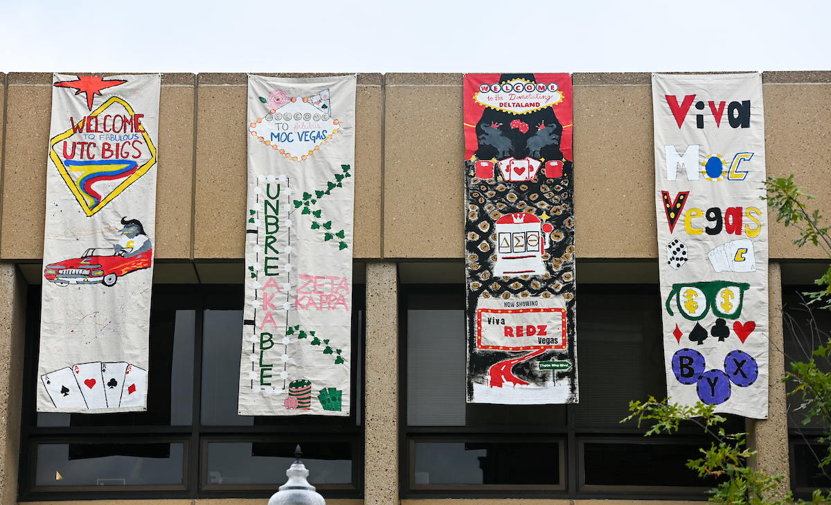 Four colorful vertical banners hang from a building, each with a Las Vegas theme featuring cards, dice, and vibrant text.