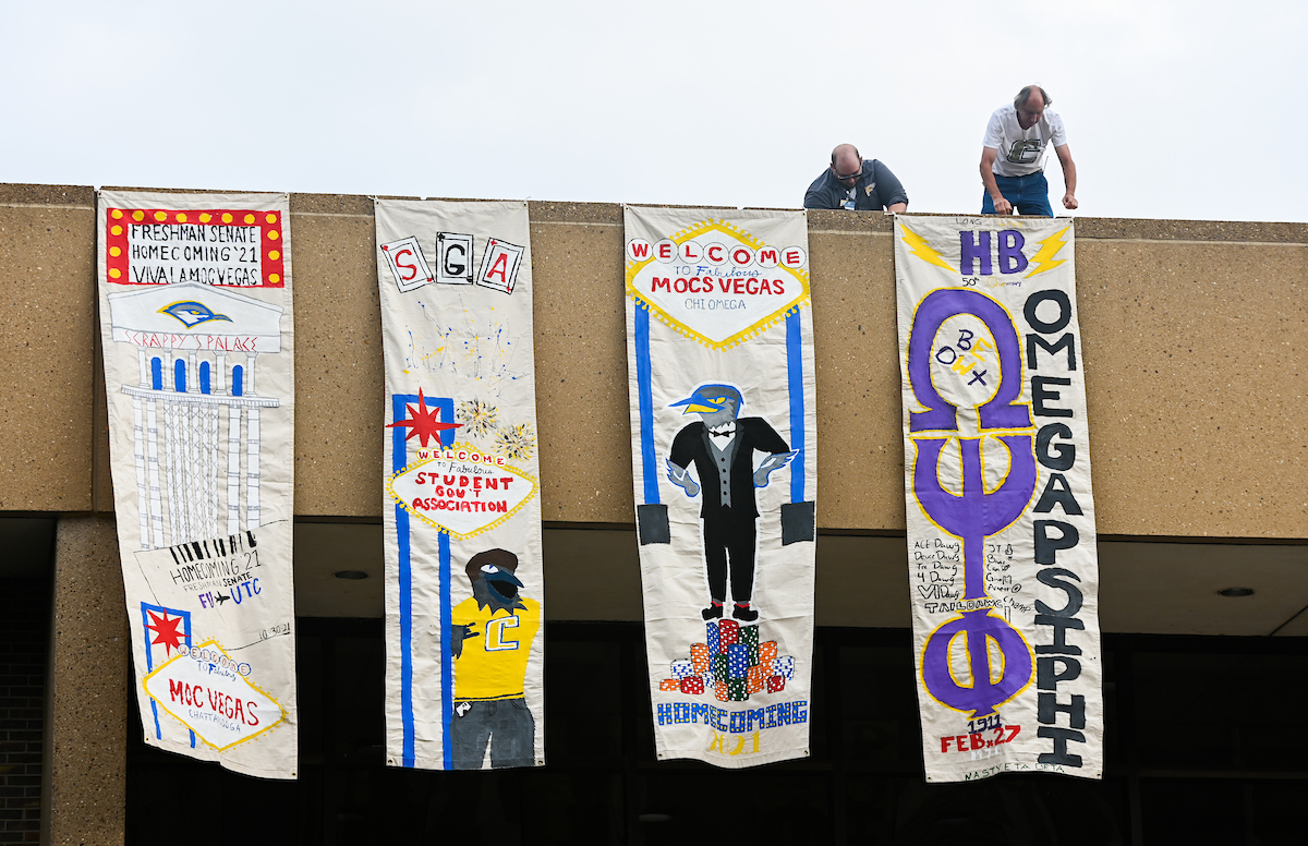 Four colorful vertical banners hang from a building, each with a student organization theme.