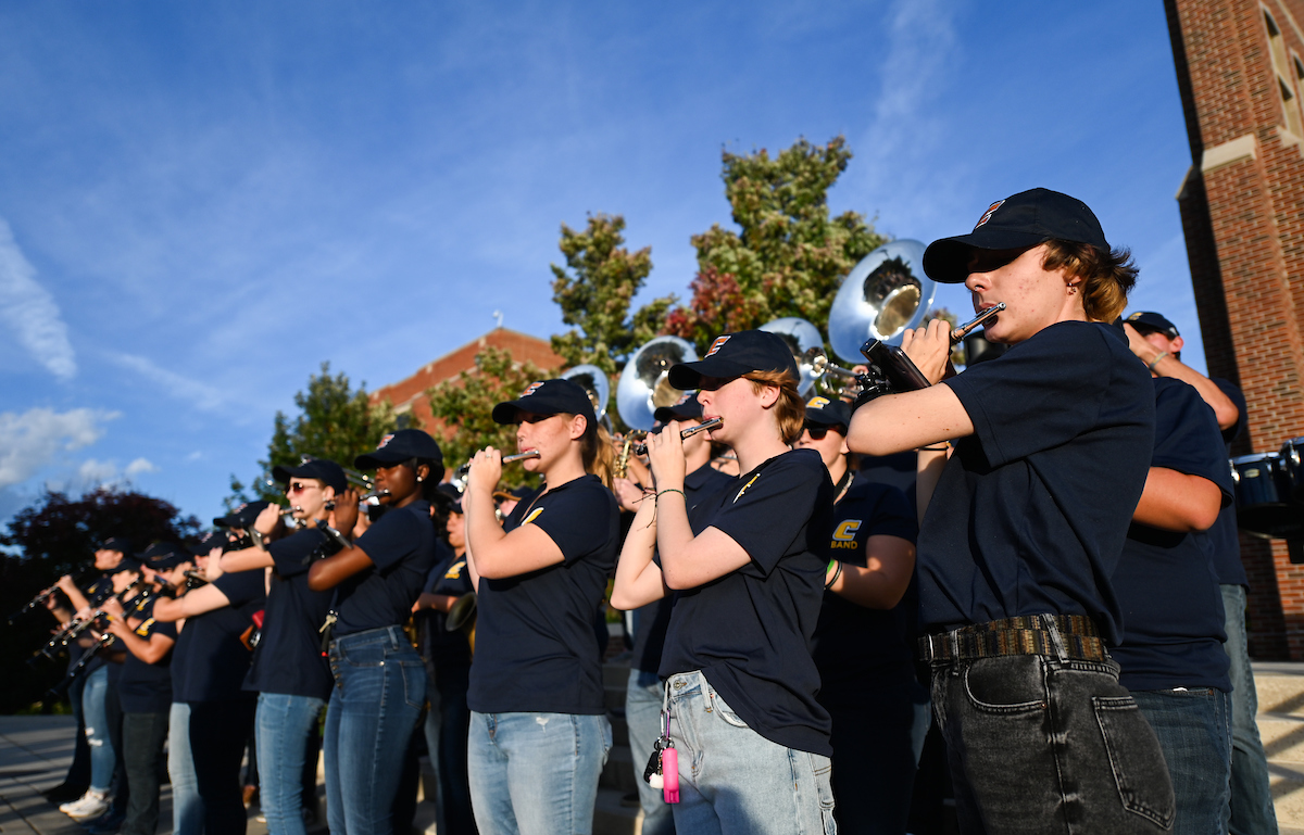 Marching Mocs play instruments on outdoor steps, wearing navy uniforms and caps.
