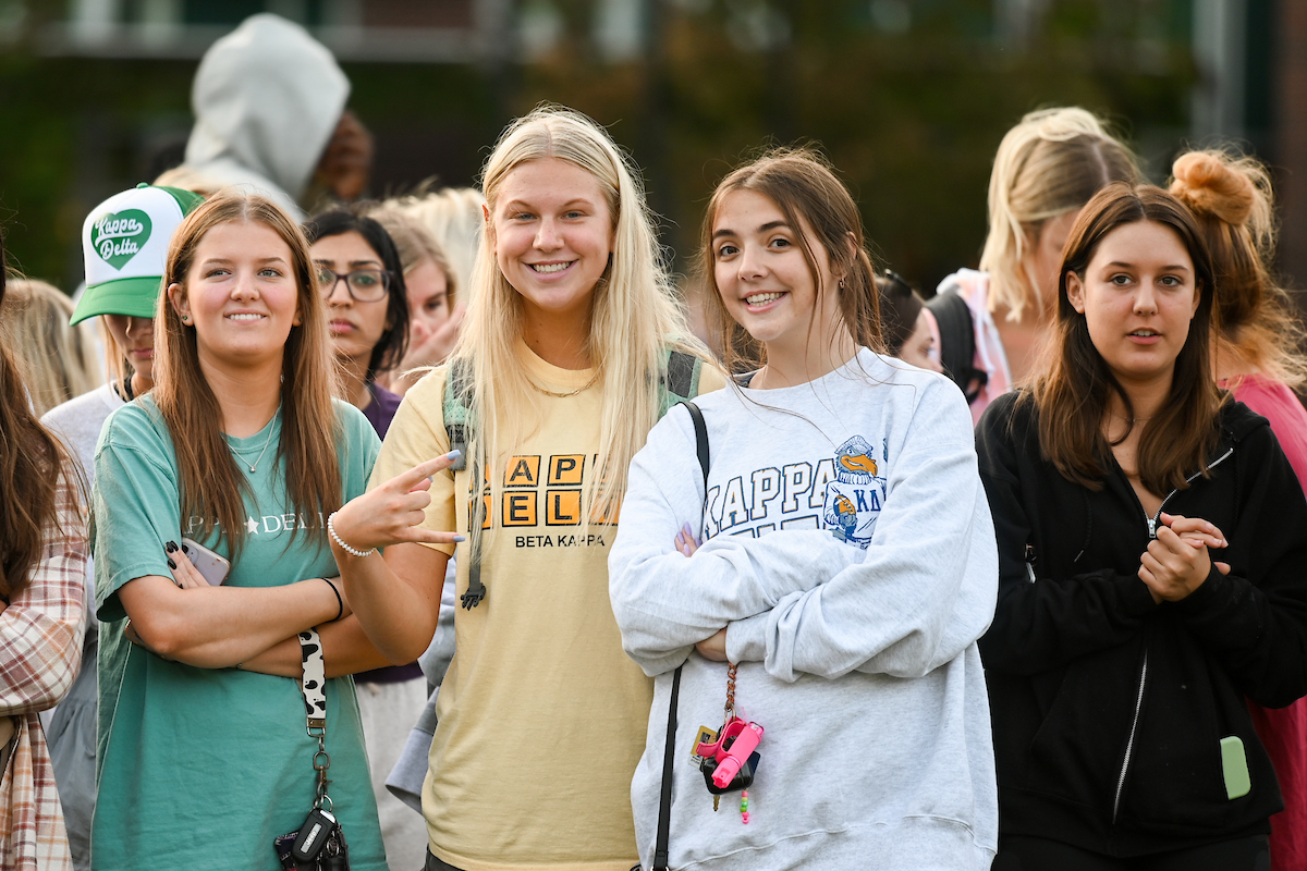 A group of smiling young women stand together outdoors, one holding up the "Power C".