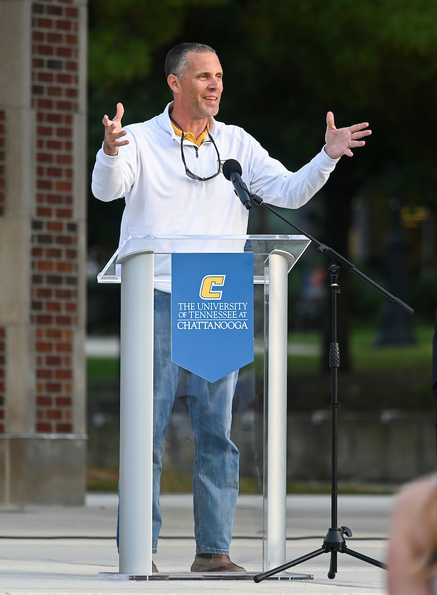 Football Coach Rusty Wright is speaking at a podium outside.