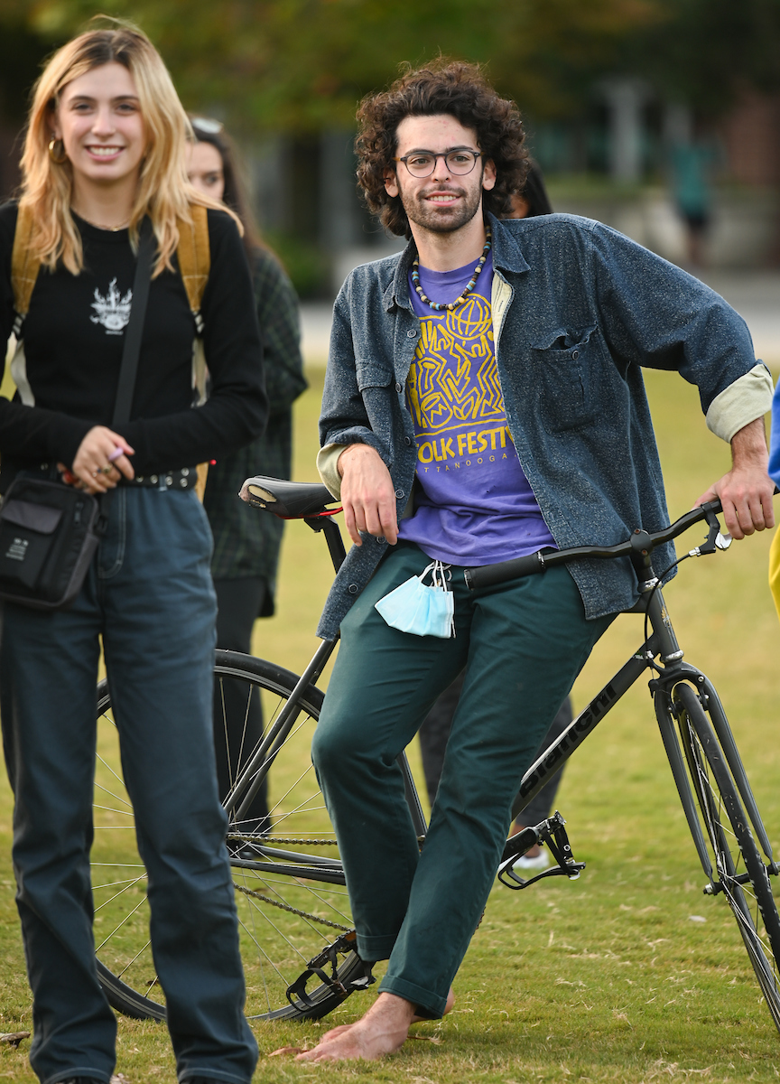 A woman smiling and a man leaning on a bicycle on grass.
