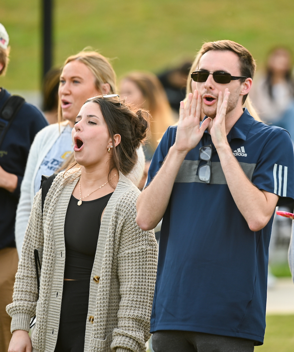 A group of people outdoors is cheering. One man cupping his mouth to cheer.