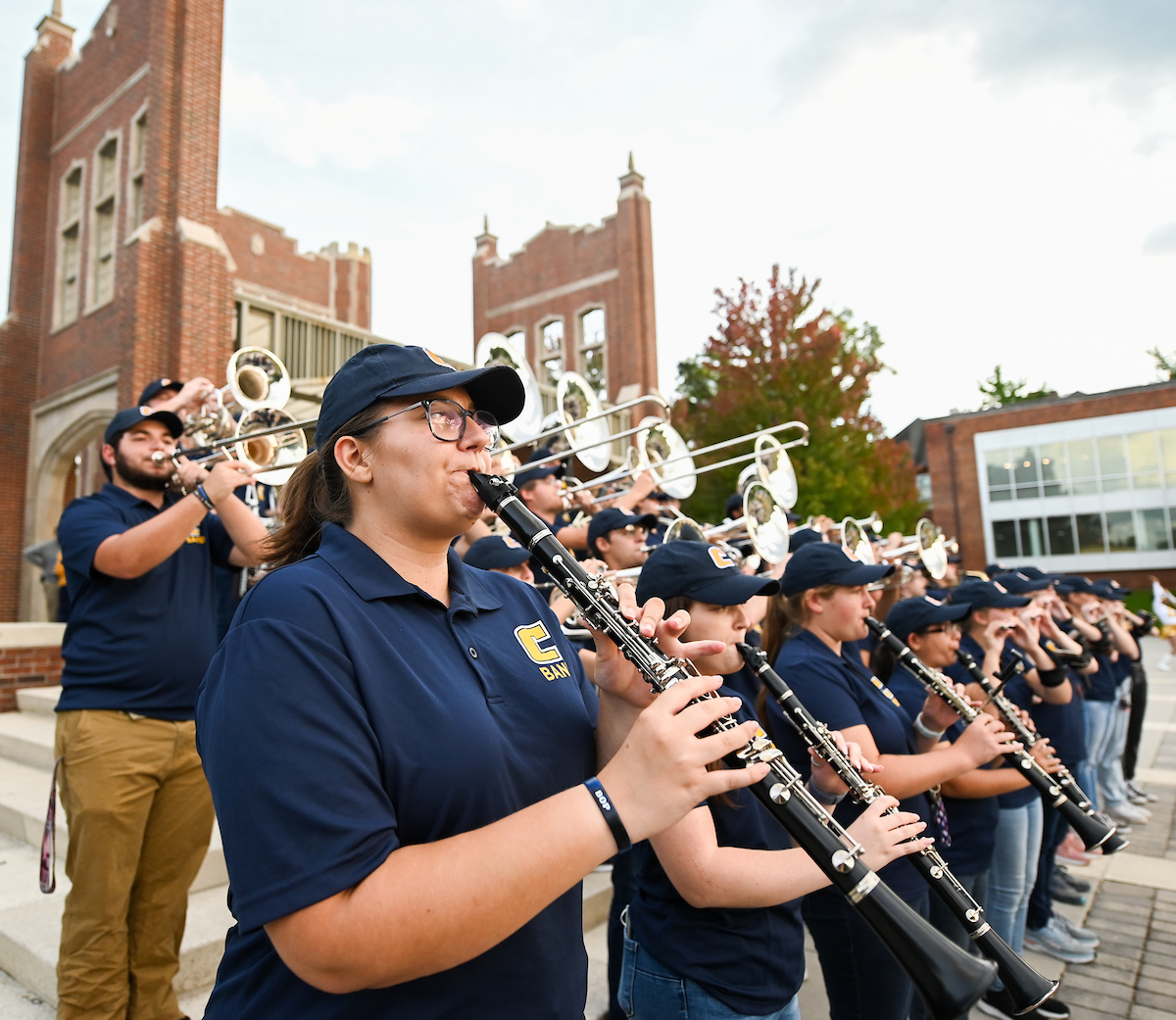 Marching Mocs play instruments on outdoor steps, wearing navy uniforms and caps.