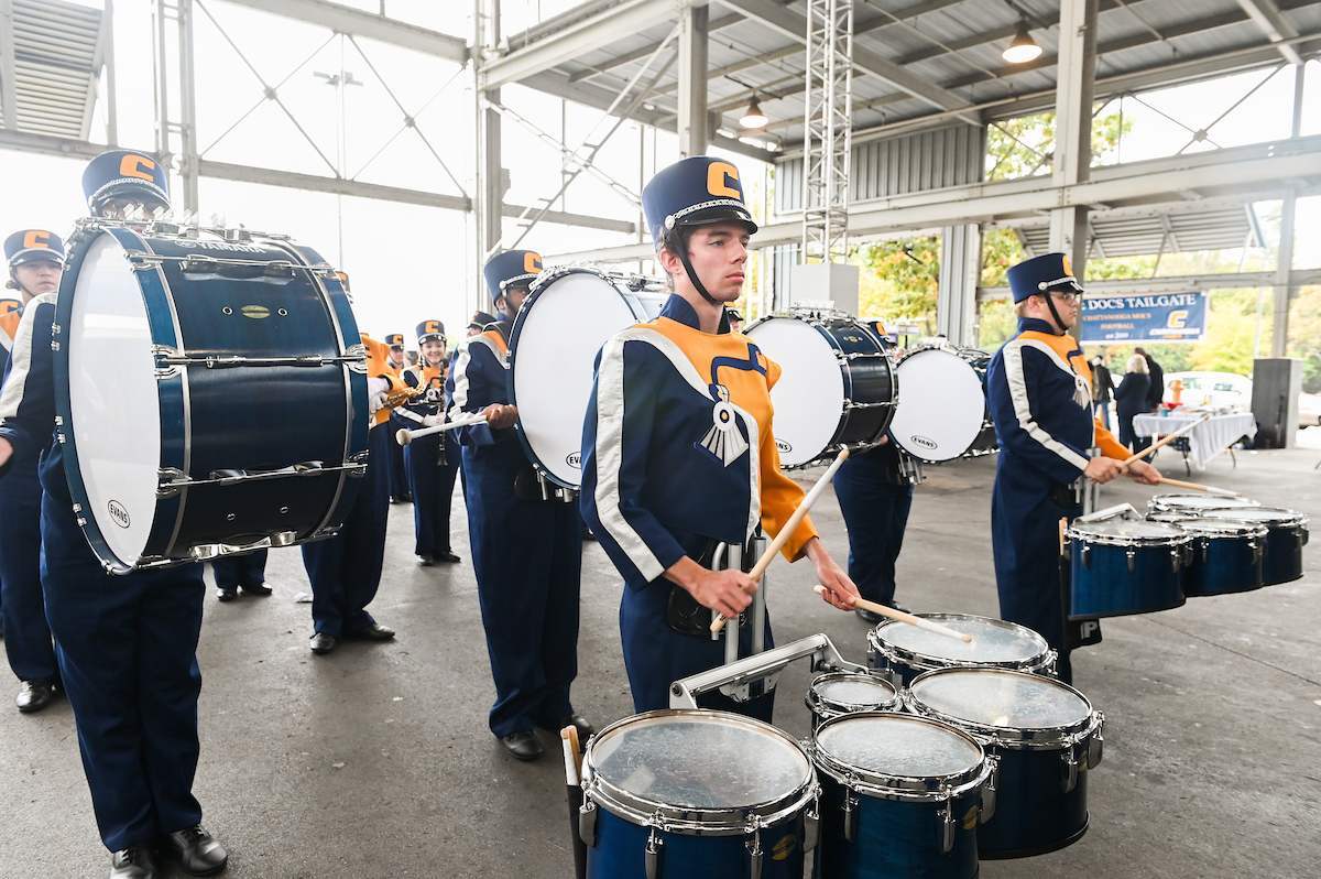 Marching Mocs in uniform play drums in open pavilion.