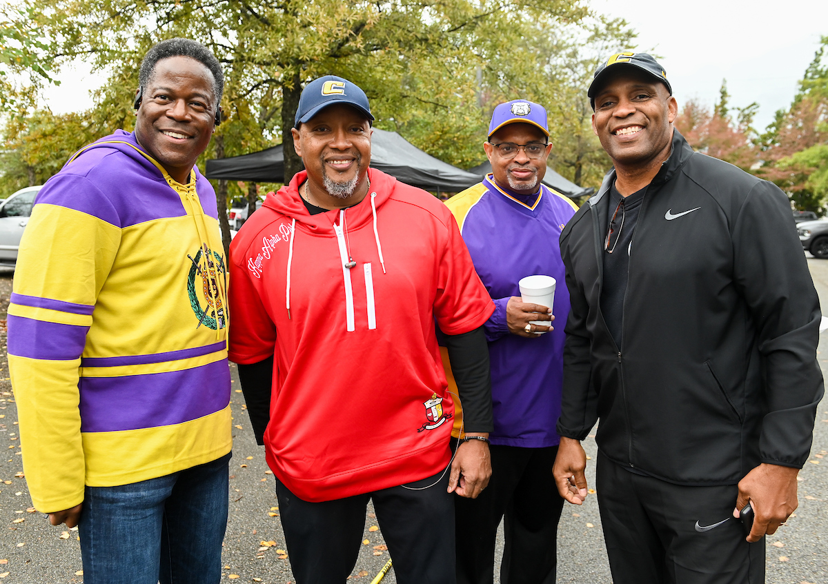 Four men smiling outdoors, wearing casual and colorful sports attire.