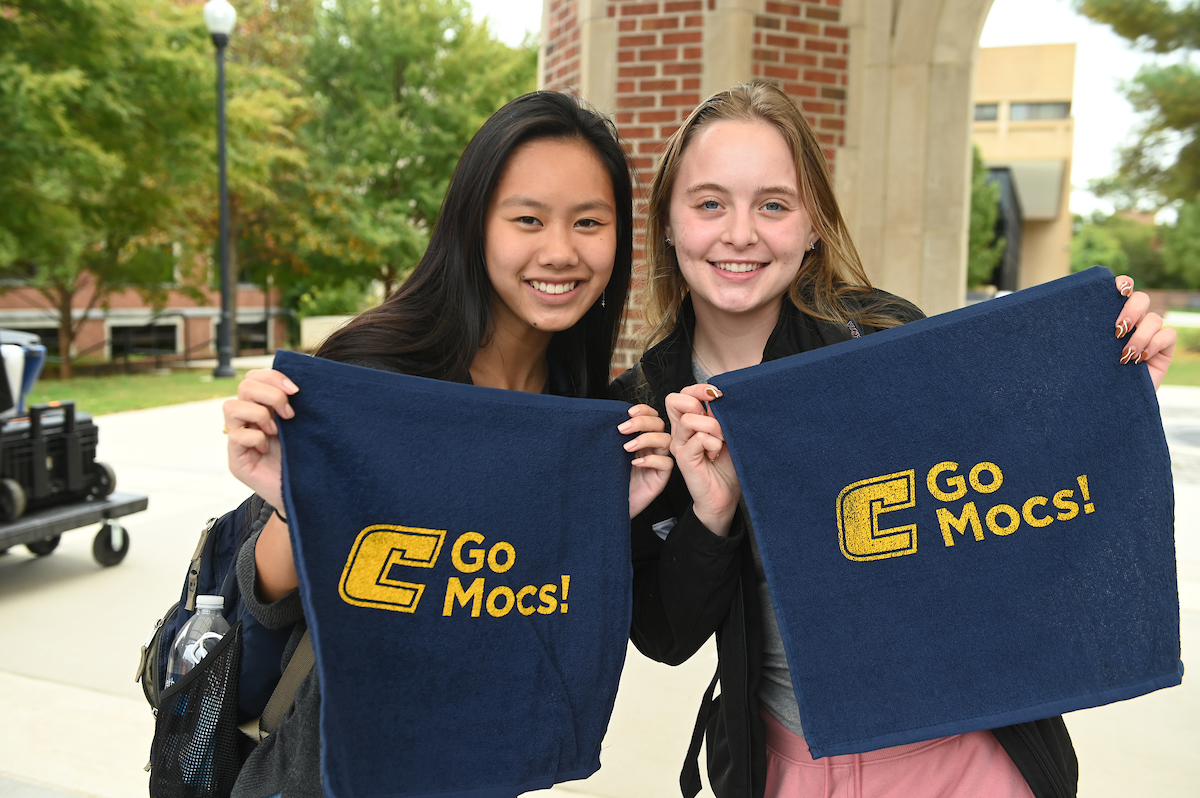 Two students smiling while holding up blue towels with yellow "Go Mocs!" text.