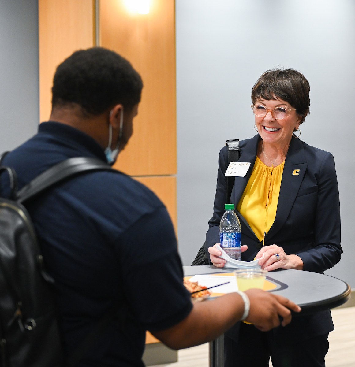 A woman in business attire smiles warmly at a man in front of her.