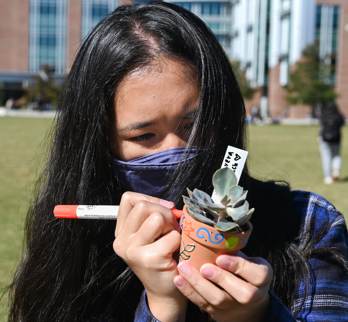A student decorates a small potted succulent with a marker.