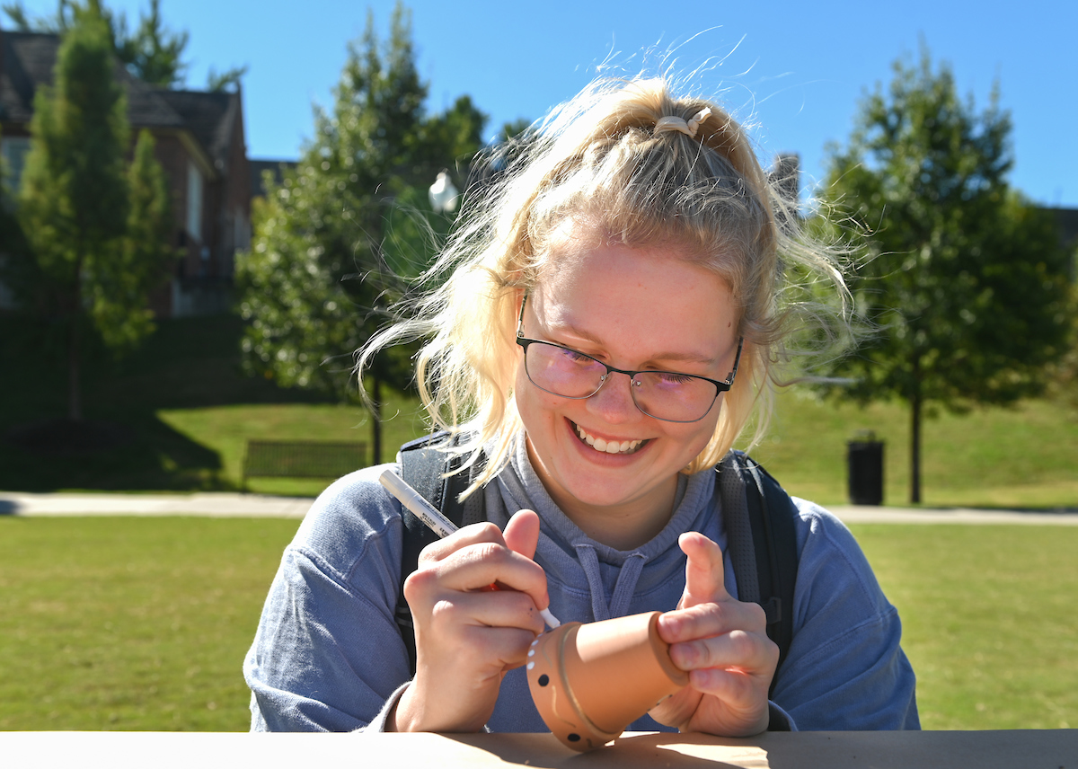 A student decorates a small pot with a marker.
