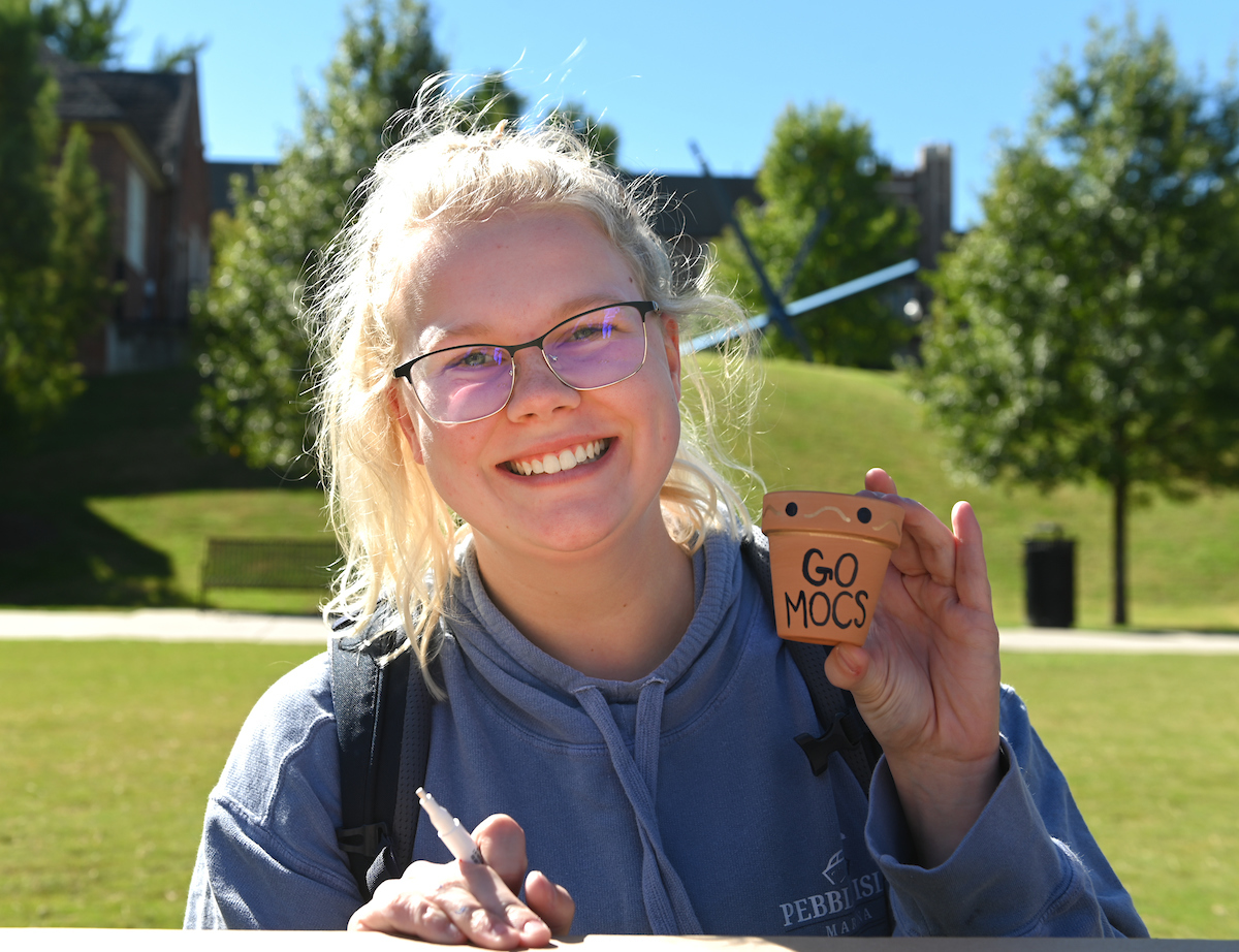 Student smiling while holding a small pot with text "Go Mocs".