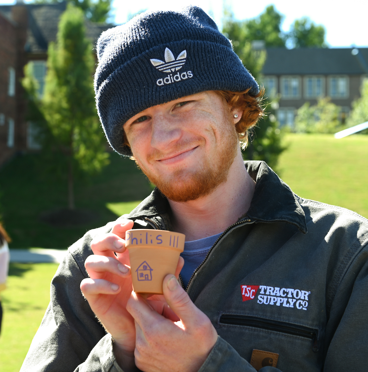 Student smiling, holding a small pot labeled "Philis III" with a house drawing.