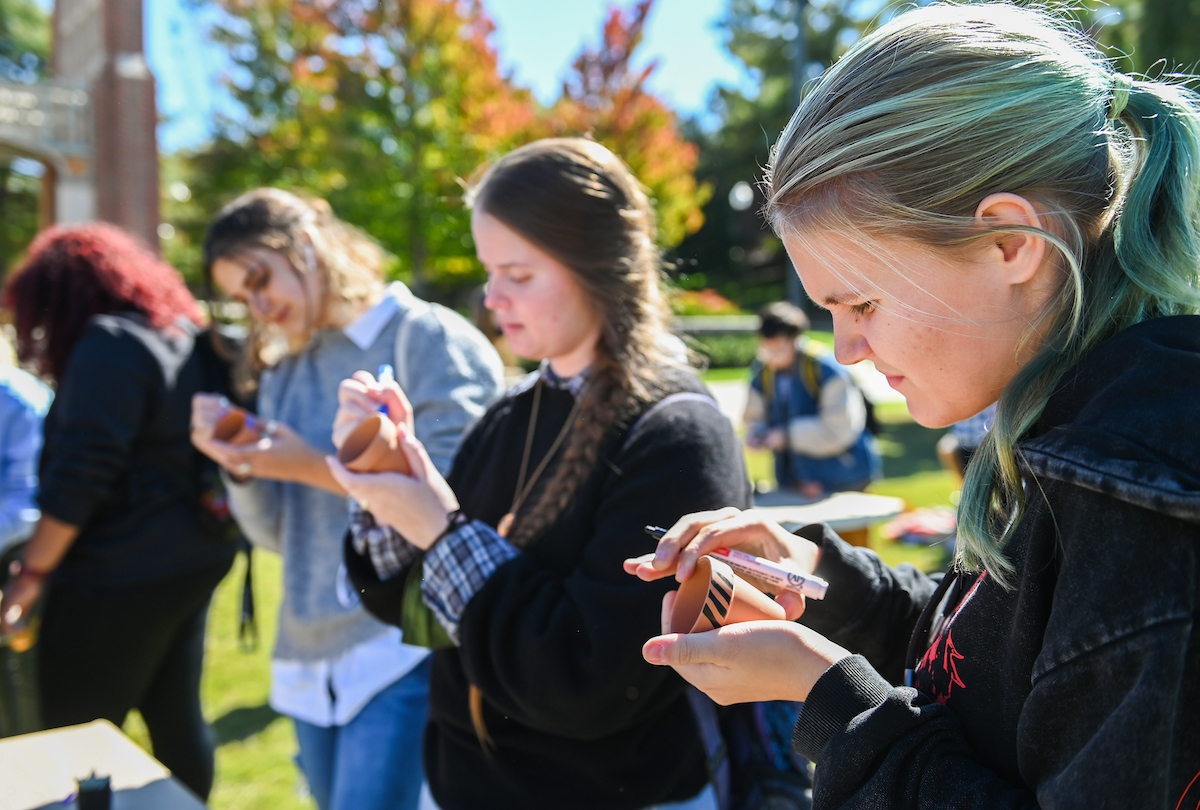 A group of students outdoors focused on decorating pottery.