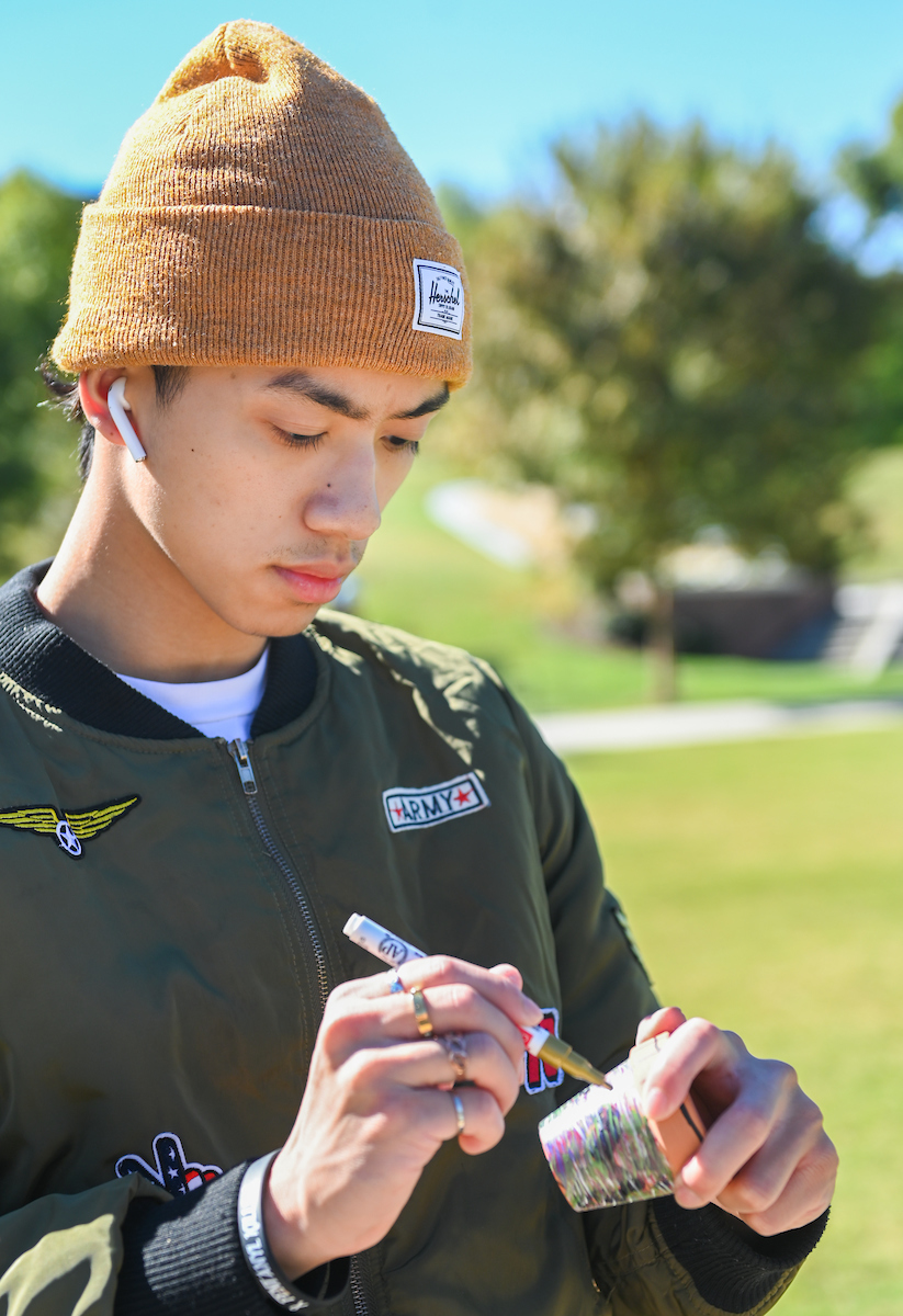Student stands outdoors, focusing on decorating a small pot.