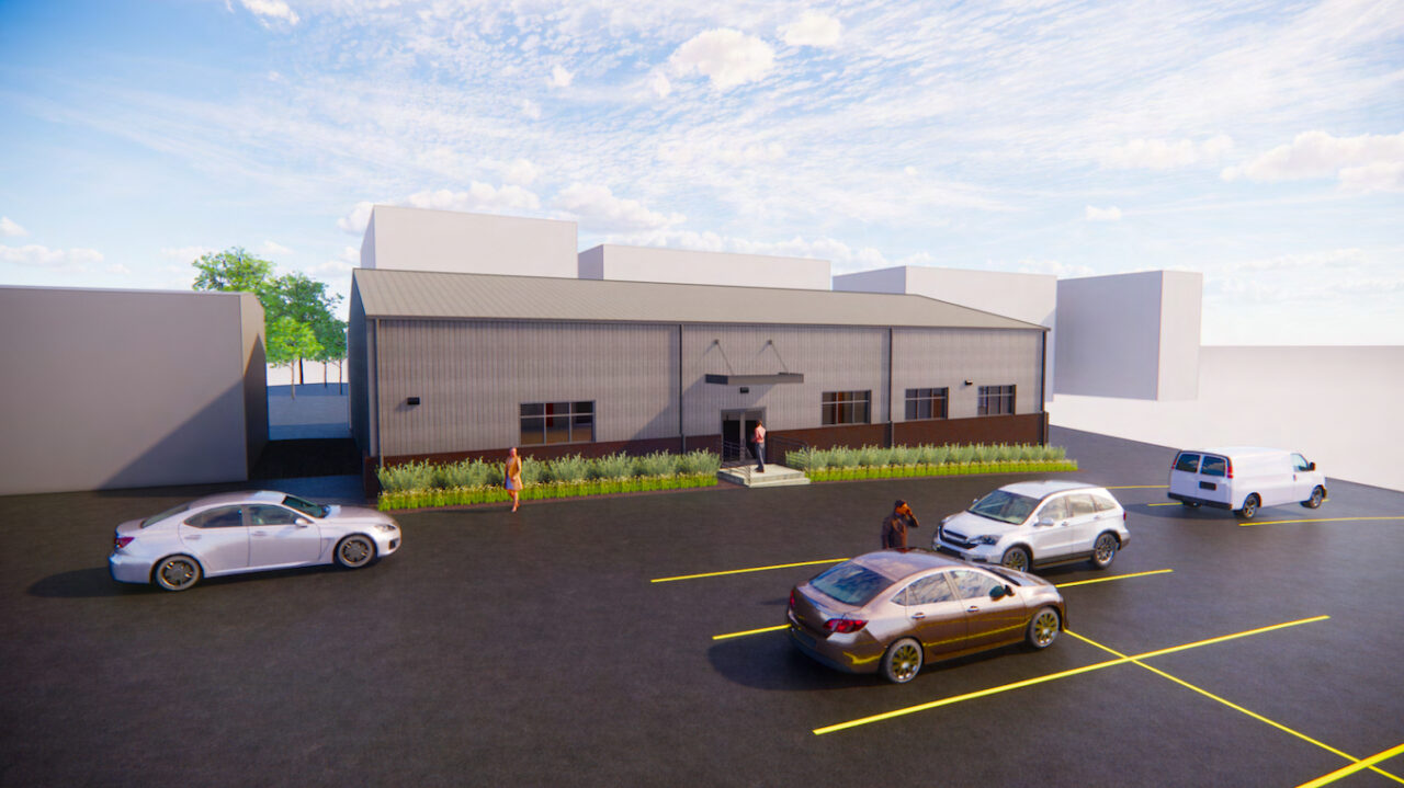 A modern, single-story gray building with a flat roof, large windows, and a front entrance is shown. Several cars are parked in a lot with marked spaces. People walk nearby, and greenery decorates the perimeter.