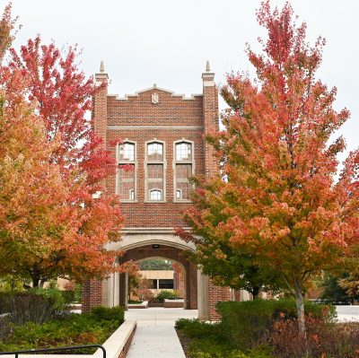 Brick building with arched entrance framed by vibrant autumn trees, displaying hues of red and orange.