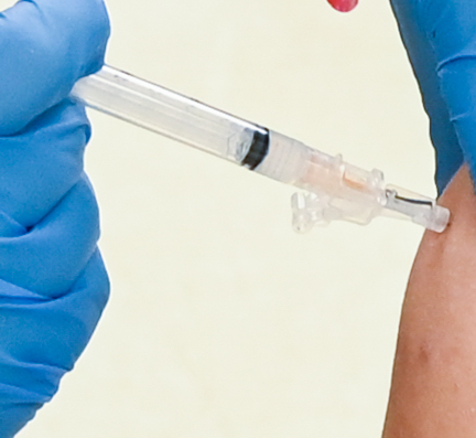 A gloved hand holds a syringe, preparing to administer an injection into an arm.