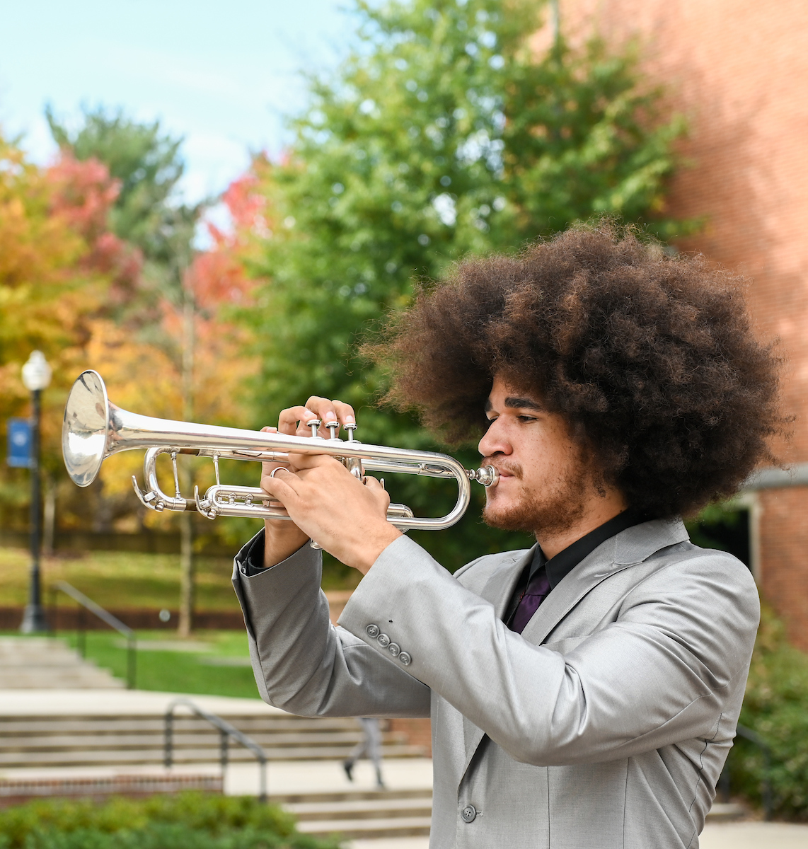A man plays the trumpet outside on campus.