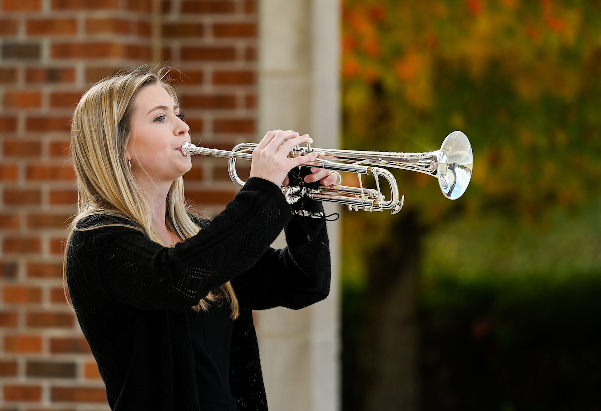 A woman plays a silver trumpet outdoors.