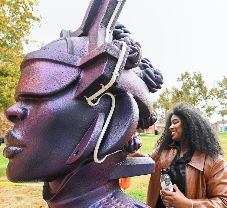 Ellex Swavoni cleans her large sculpture "Atlantis Rising" while holding a water bottle and a washcloth.