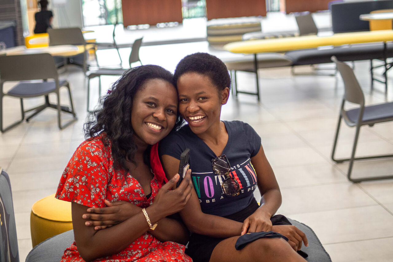 Grace Nansamba and Evelyn Namugwanyak ssmiling and sitting in a lounge area.