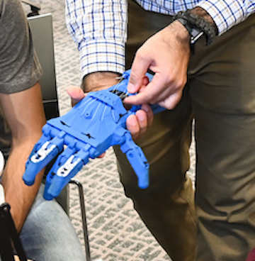 A person holds a blue, robotic hand. The hand is detailed, with visible finger joints.