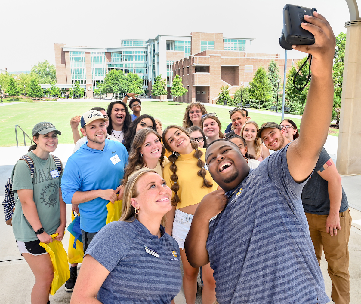 Leaders Isaiah Owens and Alexa Clements, front, pose with new students and families on Chamberlain Field during a Moc to Moc orientation tour.