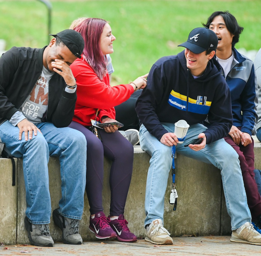 UTC students sitting outdoors, laughing and smiling.