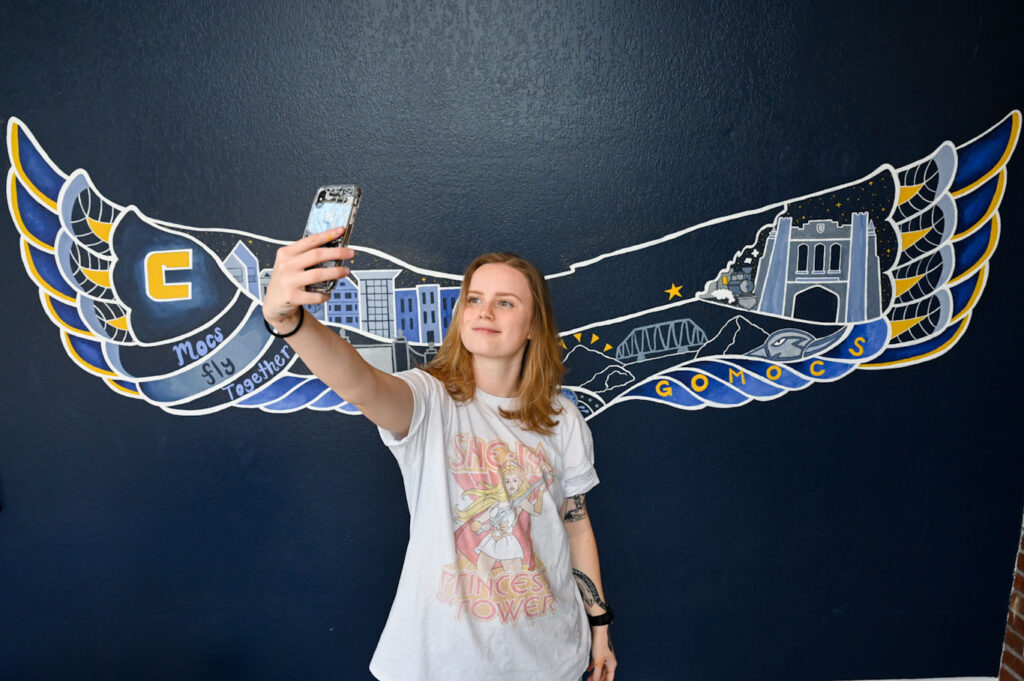 UTC junior Corinna Lingle takes a selfie in front of her mural in the lobby of the UC Foundation Apartments. Photo by Angela Foster.