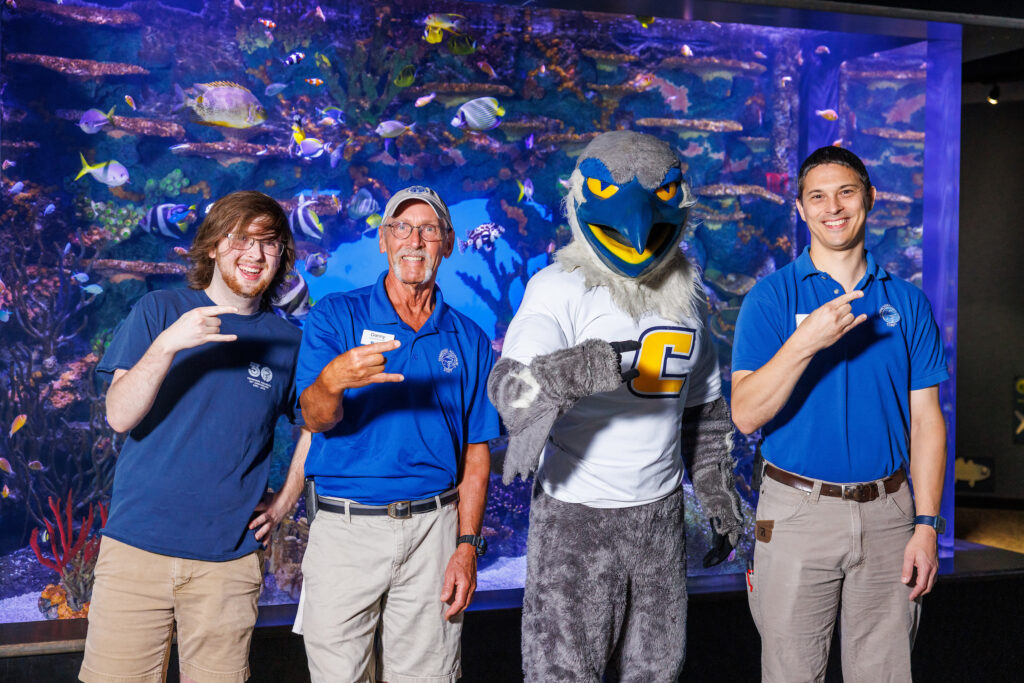 UTC student and reintroduction assistant Seth Little, left, and a pair of UTC alumni—senior aquarist Danny Alexander and curator of fishes Matt Hamilton—pose with Scrappy in front of the Indo-Pacific Reef exhibit at the Tennessee Aquarium. Photo courtesy of Doug Strickland/Tennessee Aquarium.