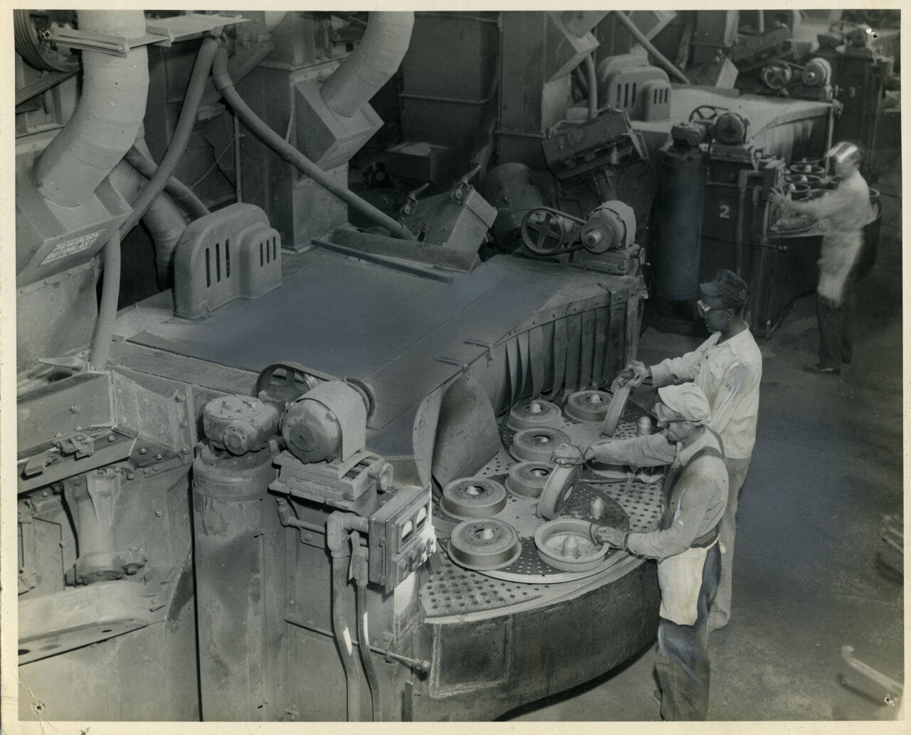 Photograph of three employees working on a factory floor. The photo is stamped with the date October 1, 1950. This is likely at Wheland Foundry, which was established in Athens, Tennessee, in 1866, and moved to Chattanooga in 1873, where the plant built sawmill machinery and oil well drilling equipment. During World War I and World War II, they made anchor windlasses for ships as well as guns and shells.
