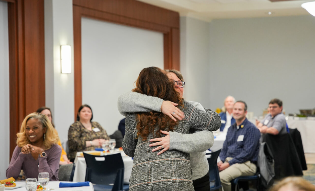 Sandra Cordell (wearing glasses) receives a hug from Katrina Craven, director of marketing and communications in the Gary W. Rollins College of Business, at the Chancellor's Blue Ribbon Award Luncheon. Photo by Jerrod Niles.