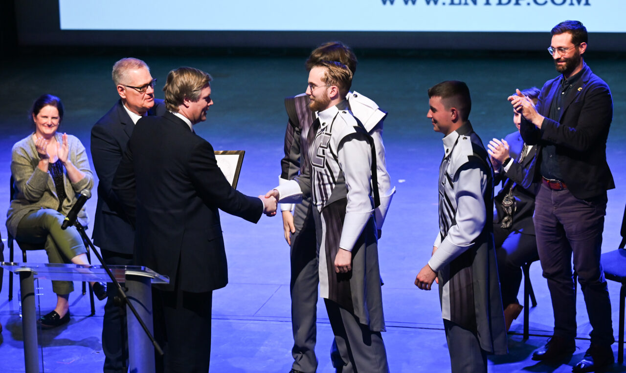 Senior Patron Duncan Sandys, former Lord Mayor of the City of Westminster, third from left, talks with UTC band members Wednesday, March 22, 2023 in the Hayes Concert Hall as he presents the Marching Mocs with their official invitation to participate in the London New Year’s Day Parade.