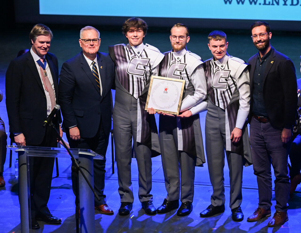Representatives from the London Parade office and the city of London talk Wednesday, March 22, 2023 in the Hayes Concert Hall while presenting the Marching Mocs with their official invitation to participate in the London New Year’s Day Parade. Left to right: Senior Patron Duncan Sandys, former Lord Mayor of the City of Westminster, Randall Coleman, director of bands, band members Justin Haynes, Matthew Warren and Dylan Campbell, and Robert Truan, assistant director of bands.