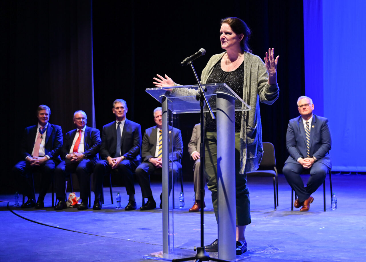 Pam Riggs Gelasco speaks Wednesday, March 22, 2023 in the Hayes Concert Hall during a ceremony in which representatives from the London Parade office and the city of London present the Marching Mocs with their official invitation to participate in the London New Year’s Day Parade.