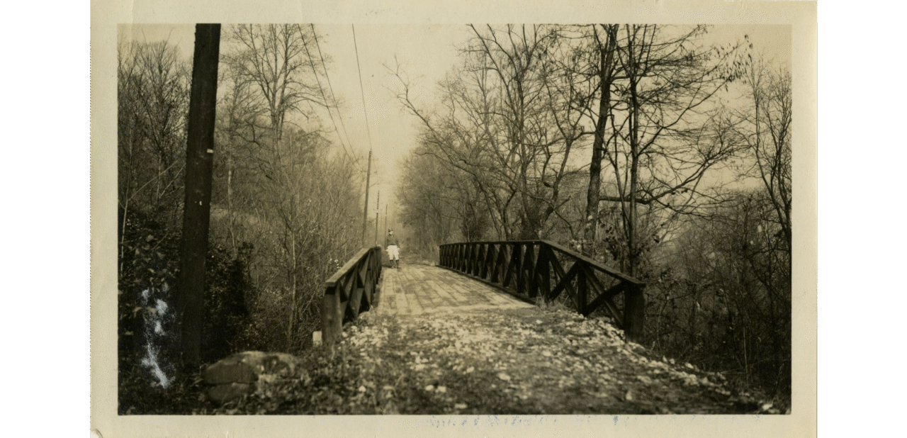 Black-and-white photograph of an unidentified Civilian Conservation Corps worker walking on a wooden bridge. 