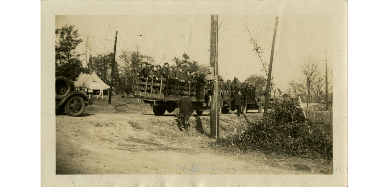 Black-and-white photograph of Civilian Conservation Corps workers riding in the beds of two trucks. 