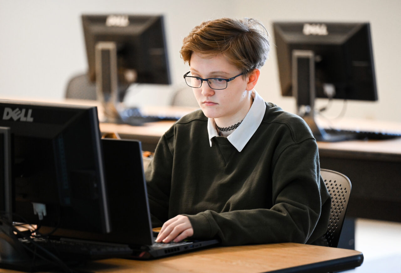 Katie Luck sits behind a computer keyboard in Assistant Professor of Practice Bill Worden’s Secure Mobile App Development class in the Engineering and Computer Science building. Photo by Angela Foster.