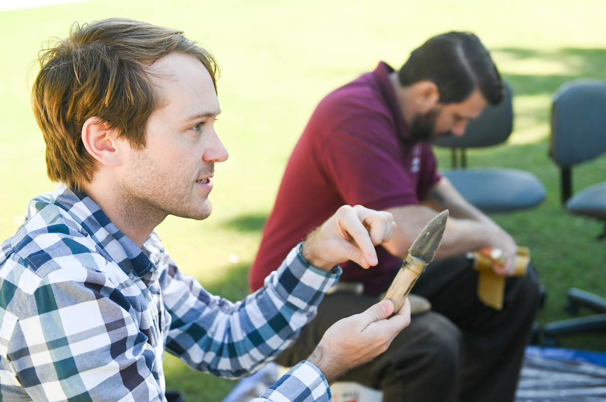 Morgan Smith teaches his Cultural Anthropology students primitive ways to make weapons on Chamberlain Field. Photo by Angela Foster.