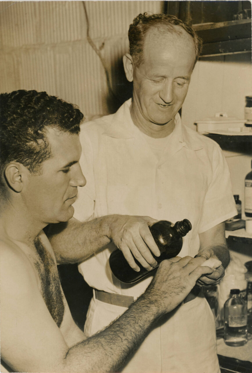 Black-and-white photograph of the Chattanooga Lookouts trainer Sandy Sandlin treating player Frank Sacka's hand in 1951.